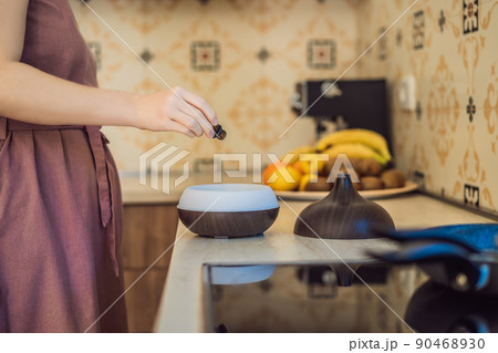 Woman adding essential oil to aroma diffuser on table Woman adding essential oil to aroma diffuser on table 90468930