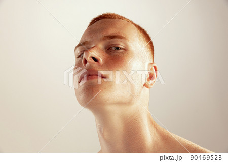 Close-up portrait of young red-haired freckled man posing isolated over grey studio background 90469523