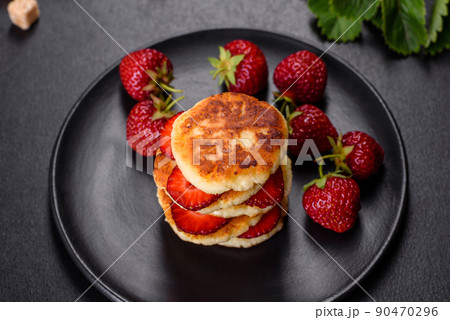 Cottage cheese pancakes with sliced strawberries and strawberry jam on a plate on a concrete background Cottage cheese pancakes with sliced strawberries and strawberry jam on a plate on a concrete background 90470296