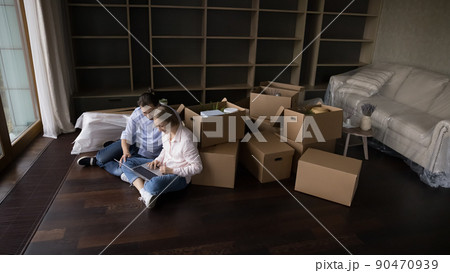 Couple use laptop seated on floor, heap of boxes nearby 90470939