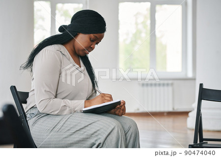Young serious black woman making notes in notebook before or after session Young serious black woman making notes in notebook before or after session 90474040