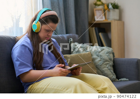 Young female with disability watching online video or movie in living room Young female with disability watching online video or movie in living room 90474122