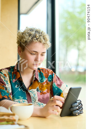 Young woman with partial arm scrolling through online videos in smartphone 90474154