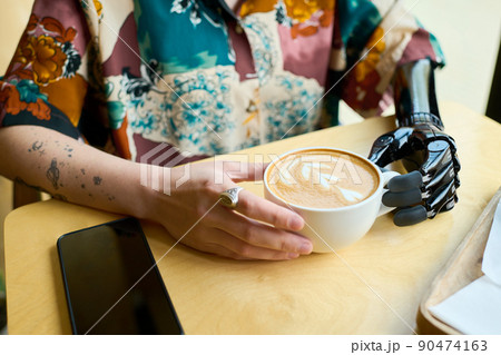 Hands of young woman with partial arm holding cup of cappuccino 90474163