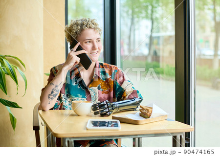 Happy young female with partial arm speaking on mobile phone in cafe 90474165
