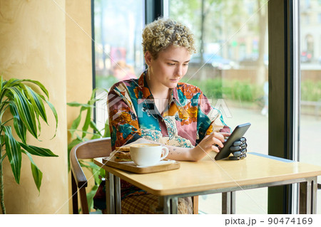 Young woman with physical impairment scrolling in smartphone in cafe 90474169