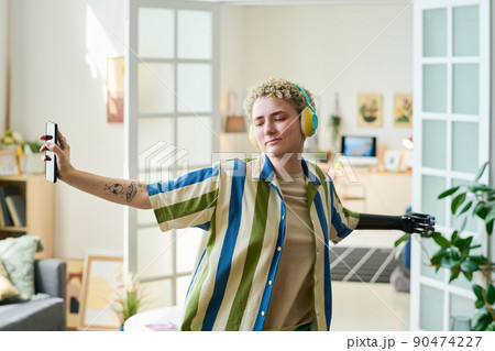 Happy young female with arm prosthesis dancing in living room at leisure 90474227