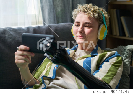 Happy girl with myoelectric arm watching online movie in smartphone on sofa 90474247