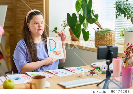 Young student with Down syndrome learning letters in front of smartphone camera Young student with Down syndrome learning letters in front of smartphone camera 90474298