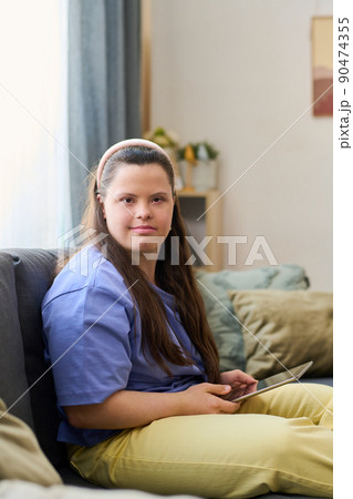 Cute girl with disability using tablet while sitting on sofa in living room Cute girl with disability using tablet while sitting on sofa in living room 90474355