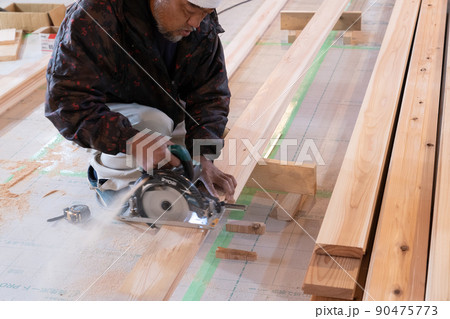 木造住宅の現場で電動ノコギリで木材の加工をする大工 90475773
