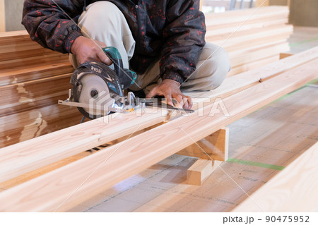 木造住宅の現場で電動ノコギリと曲尺で木材の加工をする大工 90475952