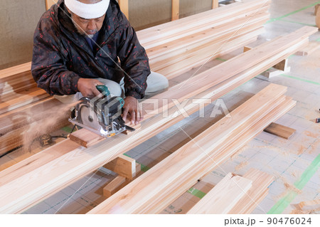 木造住宅の現場で電動ノコギリと曲尺で木材の加工をする大工 90476024