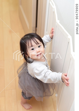 ベビーフェンスに掴まり立ちして遊ぶ1歳の女の子 90479909