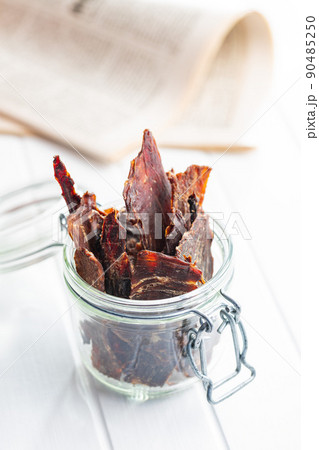 Beef jerky meat. Dried sliced meat on white table. Beef jerky meat. Dried sliced meat on white table. 90485250