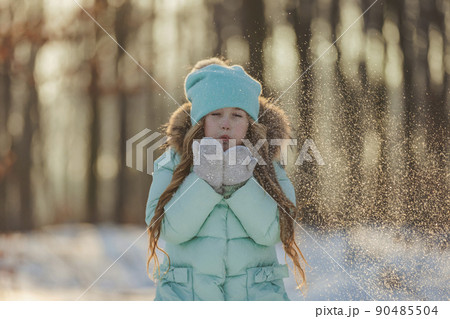 girl blows on the snow which is on her mittens 90485504