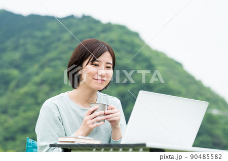 屋外でコーヒーを飲みながらパソコンを見る女性 90485582