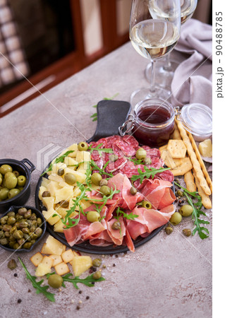 Two glasses of white wine and Italian antipasto meat platter on domestic kitchen Two glasses of white wine and Italian antipasto meat platter on domestic kitchen 90488785