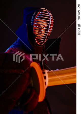 Close up shot, Kendo fighter wearing in an armor, traditional kimono, helmet practicing martial art with shinai bamboo sword, black background. 90489126