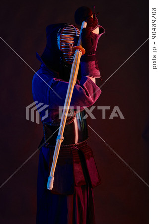 Close up shot, Kendo fighter wearing in an armor, traditional kimono, helmet practicing martial art with shinai bamboo sword, black background. 90489208