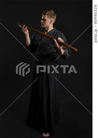 Kendo guru wearing in a traditional japanese kimono is practicing martial art with the shinai bamboo sword against a black studio background. Kendo guru wearing in a traditional japanese kimono is practicing martial art with the shinai bamboo sword against a black studio background. 90490326