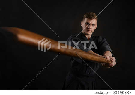 Kendo guru wearing in a traditional japanese kimono is practicing martial art with the shinai bamboo sword against a black studio background. Kendo guru wearing in a traditional japanese kimono is practicing martial art with the shinai bamboo sword against a black studio background. 90490337