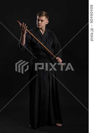 Kendo guru wearing in a traditional japanese kimono is practicing martial art with the shinai bamboo sword against a black studio background. 90490406