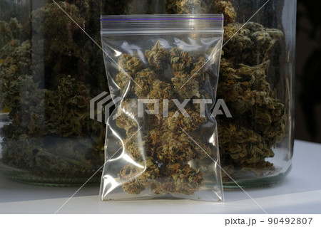 Dry and trimmed cannabis buds stored in a plastic bag on glass jars background with buds. Medical marijuana Dry and trimmed cannabis buds stored in a plastic bag on glass jars background with buds. Medical marijuana 90492807