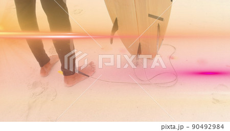 Image of pink light beams moving over feet of surfer on beach holding surfboard 90492984
