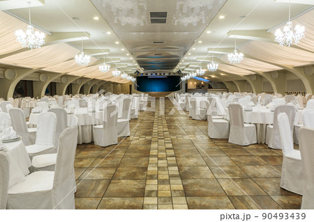 Large banquet hall decorated for social event with served tables and stage in background 90493439