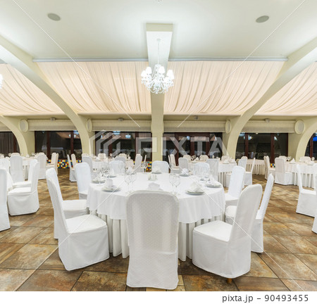 Served tables with white tablecloths arranged in banquet hall prepared for wedding reception Served tables with white tablecloths arranged in banquet hall prepared for wedding reception 90493455