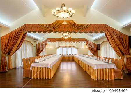 Elegant banquet hall interior in white and terracotta tones with tables prepared for festive celebration 90493462
