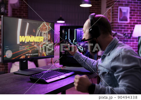Content creator winning action video games on computer, playing online gaming championship. Male player celebrating gameplay win, feeling happy about rpg tournament on computer. Content creator winning action video games on computer, playing online gaming championship. Male player celebrating gameplay win, feeling happy about rpg tournament on computer. 90494338