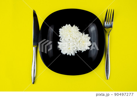 Inside the black plate there are white flowers, on the sides there are appliances on a yellow background. High quality photo Inside the black plate there are white flowers, on the sides there are appliances on a yellow background. High quality photo 90497277