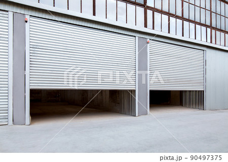 Opening gray iron shutter door of garage and industrial building warehouse exterior facade with grey concrete road, side view nobody. 90497375