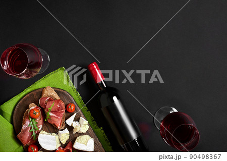 Prosciutto, salami, baguette slices, tomatoes and nutson rustic wooden board, two glasses of red wine over black background 90498367