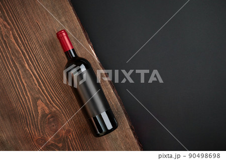 Bottle of wine on the wooden board on black background. Top view with copy space 90498698