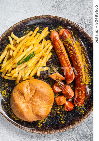 Currywurst sausages, pieces of sausage with curry sauce and French fries. White background. Top view Currywurst sausages, pieces of sausage with curry sauce and French fries. White background. Top view 90499665