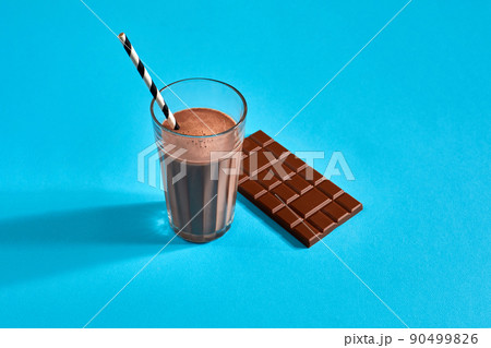 Glass of chocolate milk with chocolate bar on blue background with space for text or design 90499826