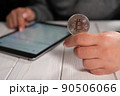 Closeup of a woman holding a silver bitcoin and working with charts on a tablet 90506066