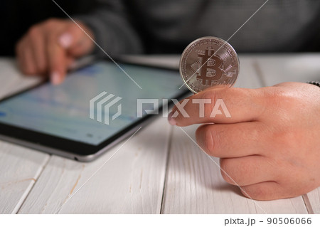 Closeup of a woman holding a silver bitcoin and working with charts on a tablet Closeup of a woman holding a silver bitcoin and working with charts on a tablet 90506066