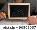 A woman holds a golden bitcoin and a blackboard with a graph. Cryptocurrency. 90506067