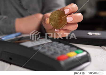 Close-up woman holding golden bitcoin coin near terminal for payment. 90506069