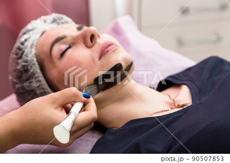 Applying a cream mask for carbon peeling on the face of an adult woman 90507853