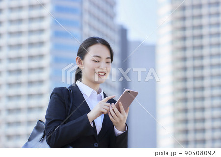 リクルートスーツの若い女性　スマホ  青空　高層ビル　笑顔 90508092
