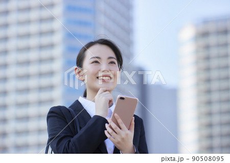 リクルートスーツの若い女性　スマホ  青空　高層ビル　笑顔 90508095