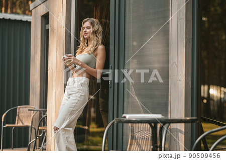 Pensive peaceful female with a coffee cup standing outdoors Pensive peaceful female with a coffee cup standing outdoors 90509456