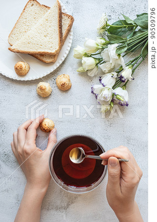 Top view of a woman's hands with a cup of tea, cookies, toasted bread, flowers Top view of a woman's hands with a cup of tea, cookies, toasted bread, flowers 90509796