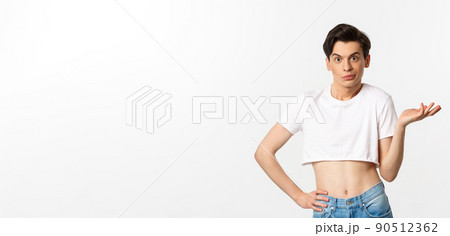Handsome androgynous man in crop top looking confused, shrugging clueless, standing over white background 90512362