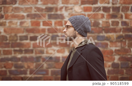 Urban style. Shot of a handsome young man in trendy winter attire standing in front of a brick wall. 90518599